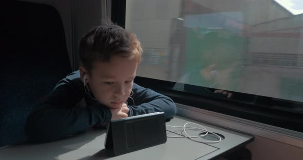 Kid with earphones watching cartoon on cell in train