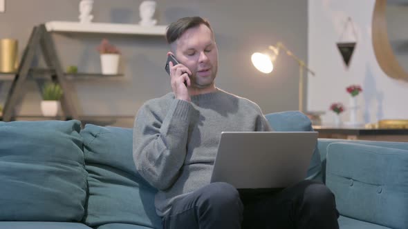 Casual Manwith Laptop Talking on Smartphone on Sofa