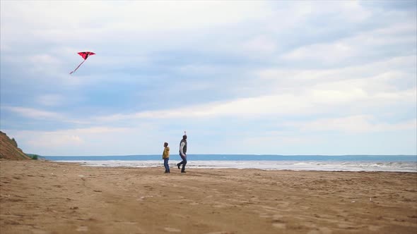 Young Dad and His Son Happily Run Along the Beach in Cold Weather with a Kite