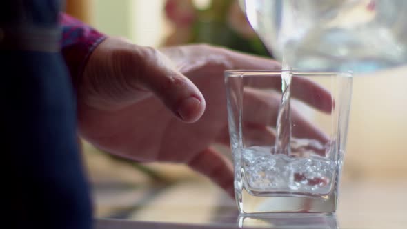 Man pouring water from a clear jug into a waterglass.