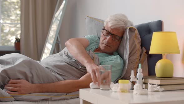 Sick Aged Man Lying in Bed Checking Temperature with Contactless Thermometer