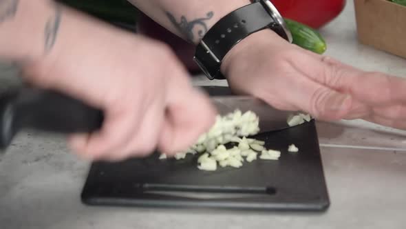 Garlic is chopped on counter top with red onion, pepper and cucumber