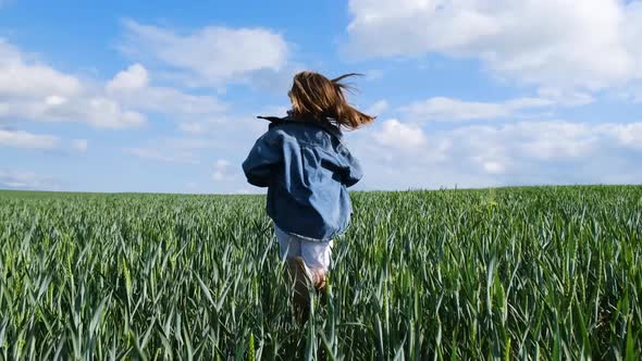 A Teenage Girl in Denim Clothes Runs Across a Wide Green Field