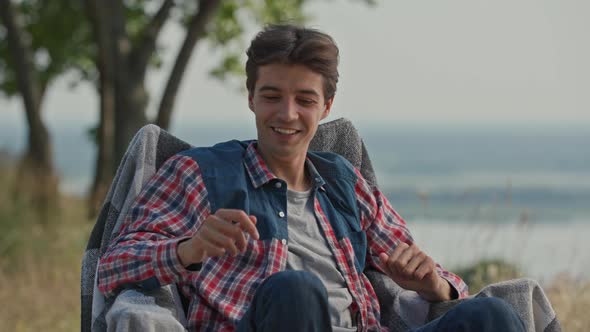 Young Adult Man Waving Hands Trying to Catch Annoying Fly in Front of His Face Sitting on Camping