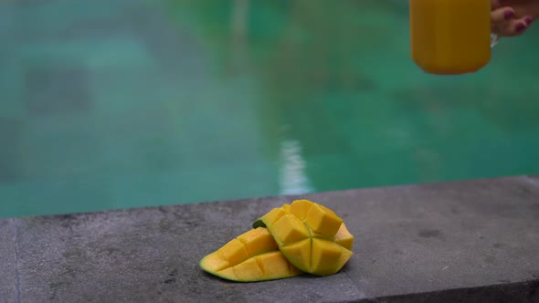 Closeup Shot of a Glass of a Mango Shake and Cut Mangoes on a Side of a Swimming Pool with a Bamboo