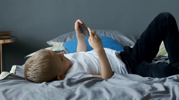 Beautiful boy playing mobile game on smartphone at home. Teenager playing mobile