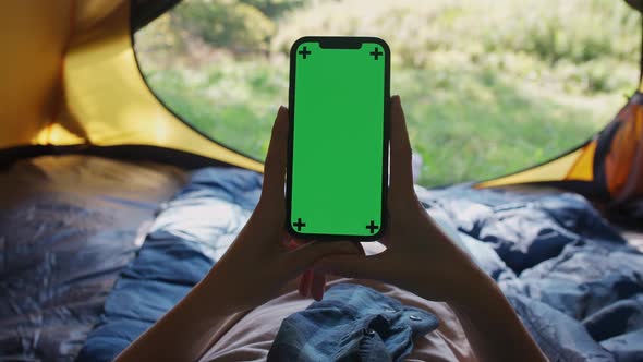 Handheld Firstperson View Female Holding a Smartphone with a Green Screen While Lying in a Tent