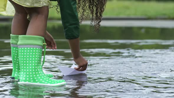 Girl Playing with Paper Boat in Puddle