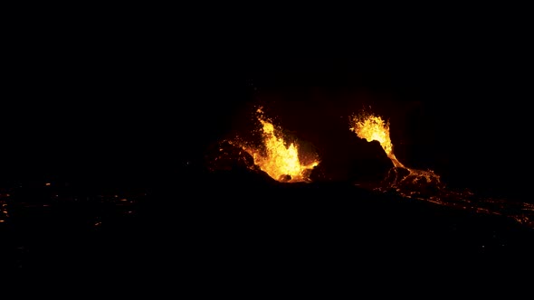 Aerial flying over an active volcano as lava spews into the dark night.