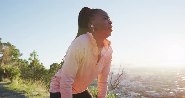 African american woman exercising outdoors wearing earphones preparing to run in countryside