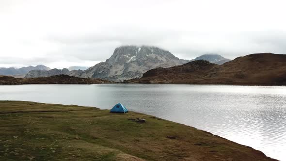Drone shot of a man waking up, going out the tent and drinking a cup of coffee near a lake on a sunn