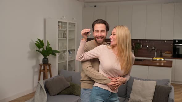 Happy Caucasian Family Couple Showing New House Keys to Camera While Posing Indoors