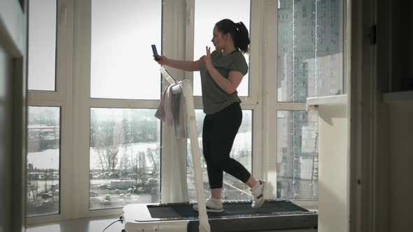 Happy smiling female is taking selfie on treadmill at home in balcony.