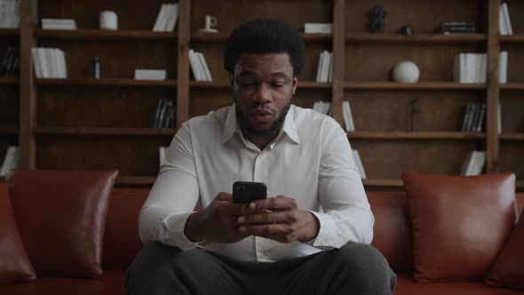 Young Adult African American Guy is Surprised While Browsing and Shopping on His Smart Phone