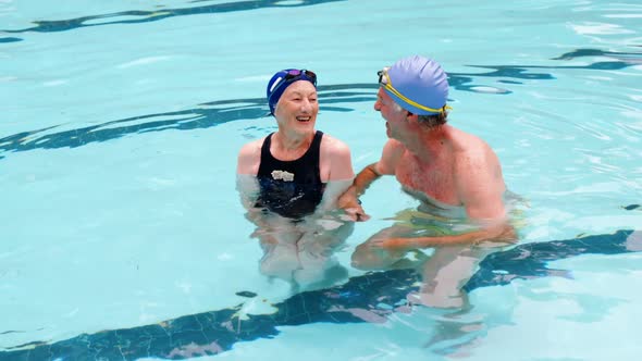 Senior couple swimming in the pool with inflatable tubes