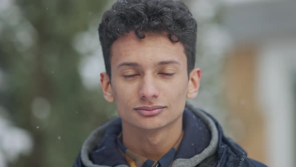 Headshot Portrait of Handsome Confident Middle Eastern Teenager Posing in Snowfall Looking at Camera