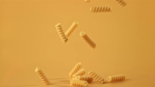 Super Slow Motion of Dry Fusilli Pasta Falls on an Orange Background