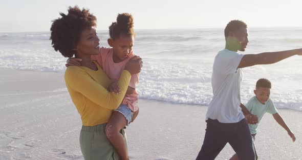 Smiling african american family walking and pointing on sunny beach