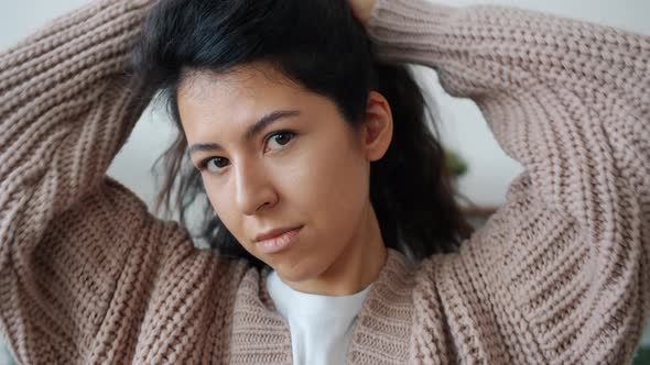 Portrait of Attractive Young Woman Fixing Hair Looking at Camera Indoors at Home