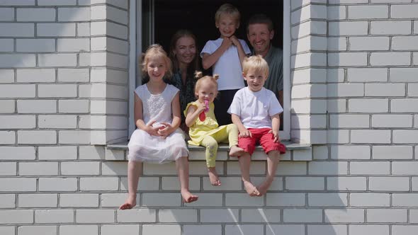 A Large Large Family Poses From the Window of Their Home.