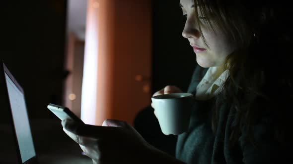 Young beautiful woman indoor at home using smart phone drinking tea