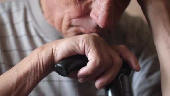 Portrait of a Caucasian sad pensive pensioner 70-80 years old sitting with a walking stick holding h