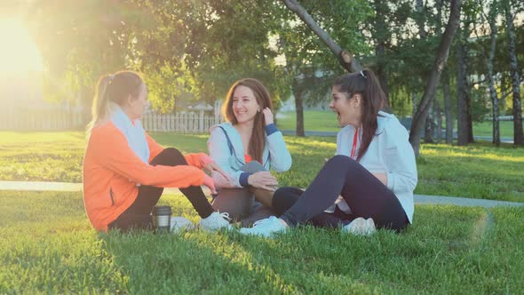 Three Friends Are Sitting on the Grass After a Morning Jog, They Laugh and Talk.