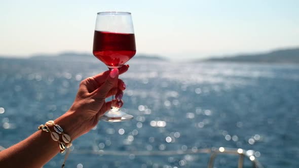 Female Hand Holding Glass of Wine on Sea Background