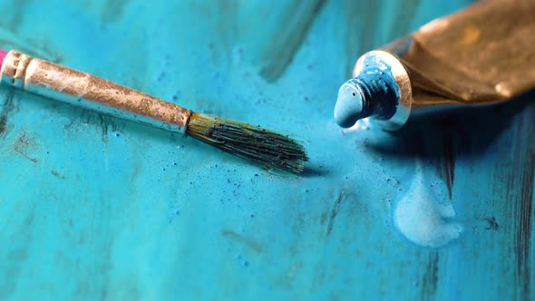 Blue color comes out of the tube. Open colored tube on floor. Paint brush paint on a blue surface