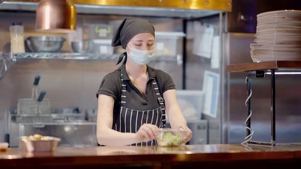 Slim Young Woman in Covid Face Mask and Apron Closing Lunch Box with Healthful Salad and Walking