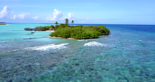 Boats visiting isolated tiny island in the edge of atoll with large coral reef and rocky sea bottom,