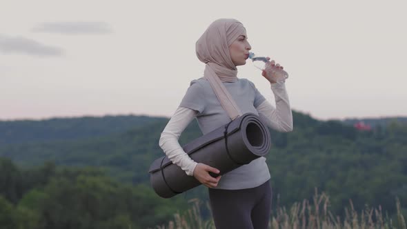 Woman in Hijab and Sport Clothes Drinking Water Outdoors