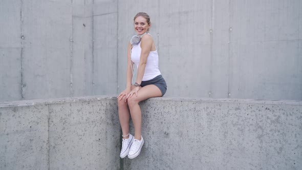 Cheerful Sportswoman Sitting on Concrete Wall