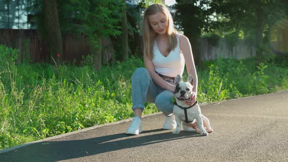 Young Woman Petting French Bulldog in Park.