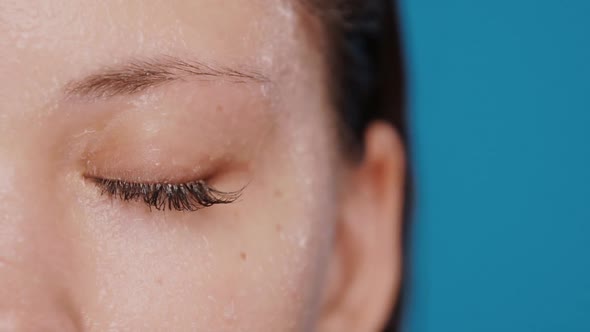 Close-up of Closed Woman Eye Getting Water Splashes Isolated on Blue