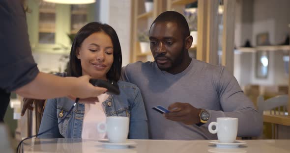 Young Mixed Race Couple Paying By Credit Card in Cafe