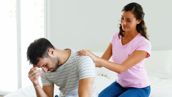 Woman comforting man sitting on bed