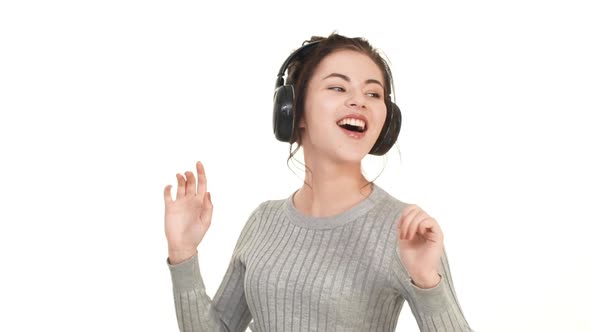 Joyful Smiling Caucasian Brunette Girl Dancing on White Background Listening Music Through Black