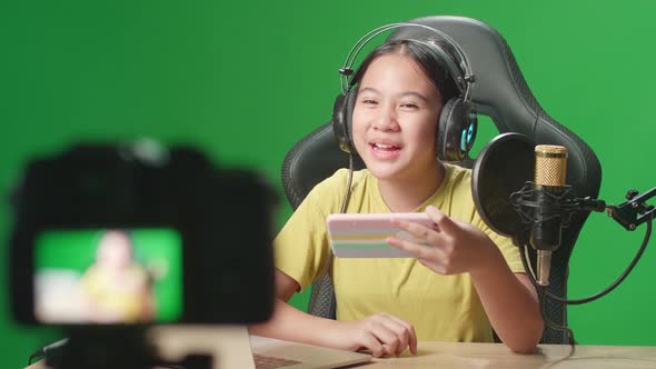 Asian Kid Girl Holding Mobile Phone And Talking To Camera While Live Stream On Green Screen