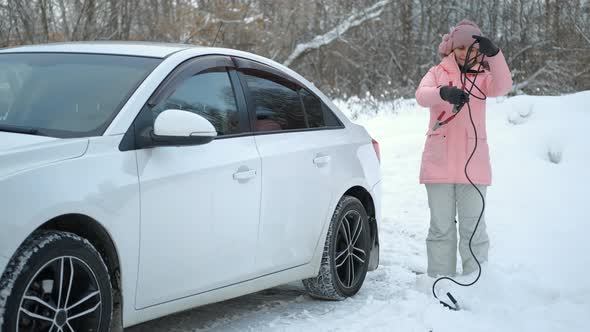 Woman with Starter Cables By the Car in Winter