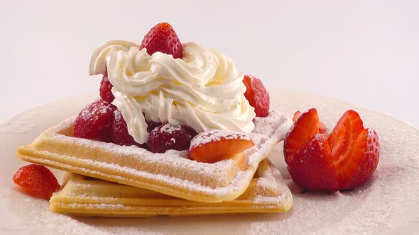 Belgian waffles with strawberry, whipped cream and powdered sugar on a plate on a white background.