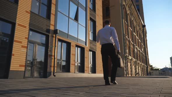 Young Businessman with Briefcase Browses Mobile Phone Going to Job on Sidewalk