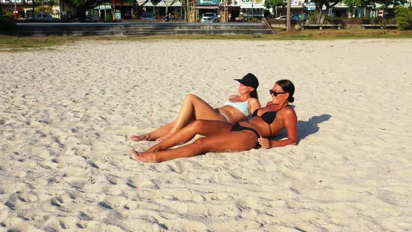 Sexy happy ladies on photoshoot having fun at the beach on sunny blue and white sand background 