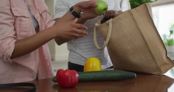 Hands of biracial couple unpacking groceries in kitchen