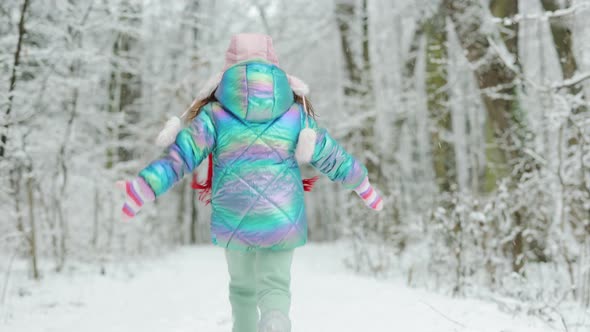 Back View Happy Laughing Child Girl Running in a Snowy Winter Park Catching Snowflakes