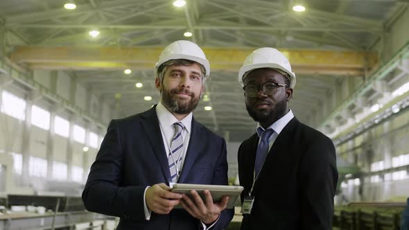 Mixed-ethnic business partners staying in helmets at building factory