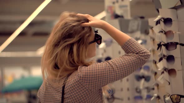 Woman Chooses Sunglasses In Supermarket. Shopaholic Girl Baying Fashion Eyewear On Retail Store.