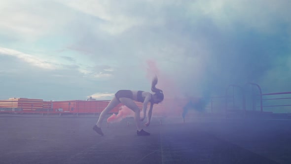 Slow Motion Female Gymnast Doing a Flip Somersault in a Smoky Space Multi Colored and Blue Smoke