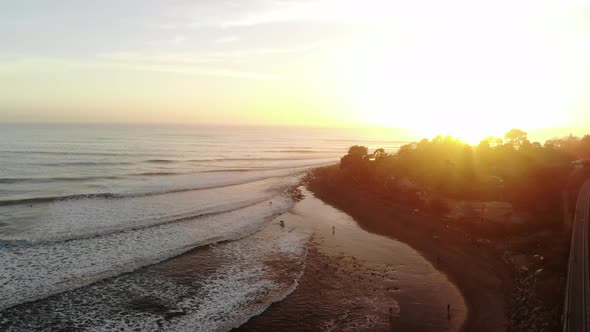 Aerial drone shot over Rincon Point surf break with ocean swell rolling in and waves crashing at sun