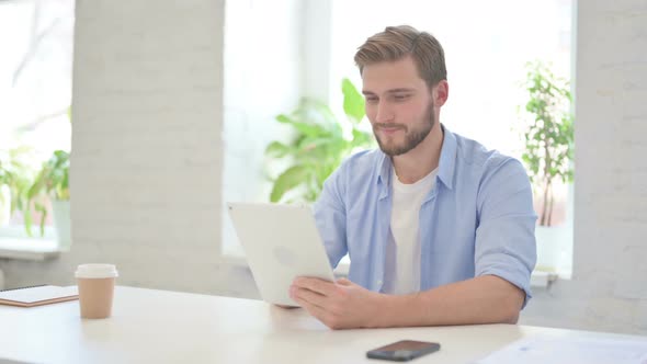 Attractive Young Creative Man Using Tablet in Modern Office